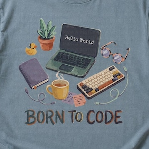 Può includere: Una t-shirt blu polvere con una stampa grafica di un computer portatile con il testo Hello World sullo schermo, una pianta in vaso, una papera di gomma gialla, un taccuino viola, una tazza gialla, occhiali e il testo BORN TO CODE.