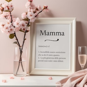 Peut inclure: Un cadre blanc avec le mot italien "Mamma" et une définition. Il est posé sur une surface blanche, avec un vase de fleurs roses et une coupe de champagne, créant une ambiance douce et féminine.