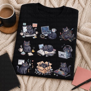 May include: A black t-shirt featuring a graphic print of nine cartoon black cats engaged in various activities, including typing on laptops, playing with computer cables, wearing headphones, sleeping on books, and sitting in a cardboard box.