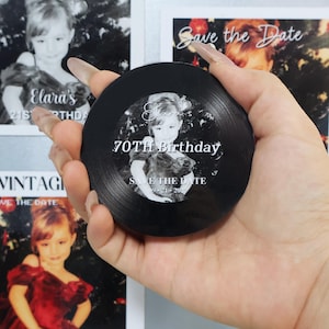 May include: A circular black vinyl record-style coaster featuring a central black and white photograph of a child. The text reads Elara's 70TH Birthday SAVE THE DATE 09-21-2027 in white lettering, mimicking the appearance of a vintage music record.