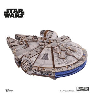Könnte beinhalten: Detailliertes Holzmodell des Raumschiffs Millennium Falcon aus Star Wars. Das Modell ist hauptsächlich grau mit braunen und blauen Akzenten und weist komplizierte Verkleidungen und kreisförmige Lüftungsöffnungen auf. Die Star Wars- und Disney-Logos sind sichtbar.
