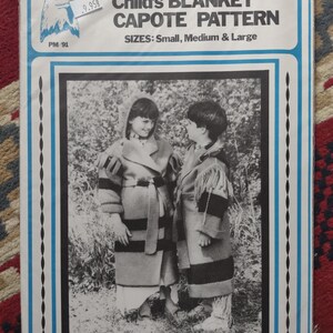 May include: A sewing pattern envelope titled Child's BLANKET CAPOTE PATTERN for sizes Small, Medium & Large. The white package features a blue border and a black and white photograph of two children wearing hooded, belted coats with striped patterns.