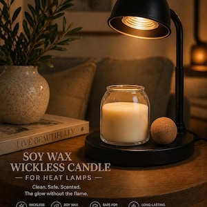 May include: A black metal candle warmer lamp with a downward-facing light bulb, positioned over a clear glass jar containing white soy wax. The base features a small cork sphere. Text reads: SOY WAX WICKLESS CANDLE FOR HEAT LAMPS. Dimensions: 10 cm tall by 9 cm wide.