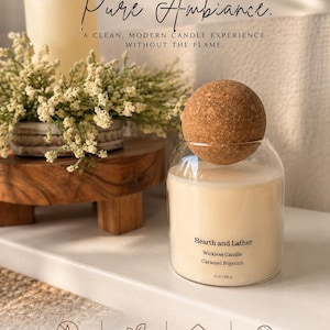 May include: A clear glass jar candle with a round cork lid, labelled Hearth and Lather Wickless Candle Caramel Popcorn 21 oz | 595 g. Text reads WICKLESS. WORRY FREE. Pure Ambiance. A CLEAN, MODERN CANDLE EXPERIENCE WITHOUT THE FLAME.