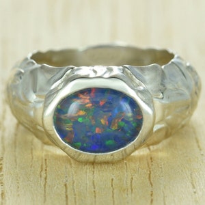 May include: A silver ring with a textured band and a blue, green, and red opal gemstone.