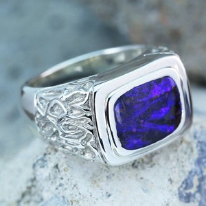 May include: A silver ring with a large, rectangular, purple opal gemstone set in a bezel setting. The band of the ring has a textured design.