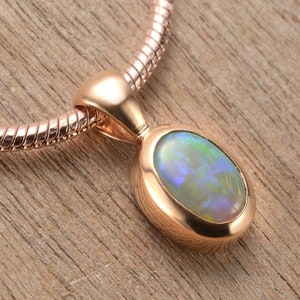 May include: A rose gold pendant necklace featuring an oval opal gemstone. The opal displays a light green, blue, and white iridescent sheen.
