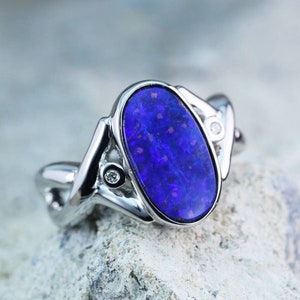 May include: A silver ring with a large oval-shaped blue opal gemstone set in a twisted band. Two smaller diamonds are set on either side of the opal.