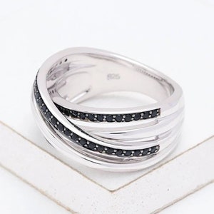 Peut inclure: Une bague en argent avec plusieurs bandes entrelacées, accentuées de pierres de zircone cubique noires.