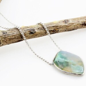 May include: A silver chain necklace with a green and white agate pendant. The pendant is set in a silver bezel.