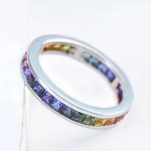 May include: A silver band ring with a rainbow of square-shaped gemstones set in a continuous line around the band.