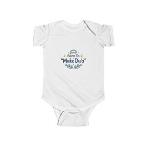 May include: White baby onesie with short sleeves. The onesie features the text "Born To Make Du'a" in a decorative font, with a crescent moon and leaf design. The onesie is designed for infants and toddlers.