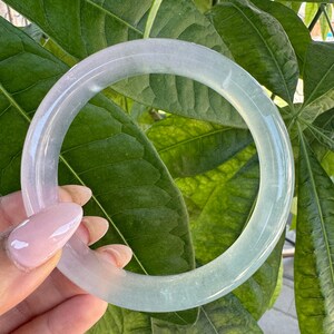 May include: A smooth, circular bangle bracelet crafted from translucent, polished stone. The material displays a subtle gradient of pale lavender and soft mint green hues, featuring a glossy, reflective surface that catches the light.
