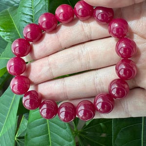 May include: A stretch bracelet composed of numerous smooth, round, deep magenta-colored beads. The beads are uniform in size and shape, featuring a polished, glossy finish that reflects light across their spherical surfaces in a circular arrangement.