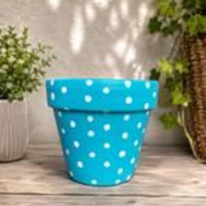May include: A bright turquoise flower pot featuring a repeating pattern of small white polka dots. The pot has a wide, flat rim at the top and a tapered body that narrows towards the base, providing a simple and functional container for plants.