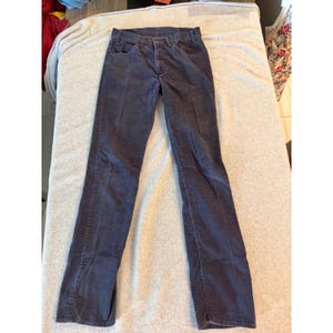 May include: A pair of dark charcoal gray corduroy pants featuring a classic five-pocket design, a button and zipper fly closure, and a straight-leg cut. The fabric has a visible vertical ribbed texture throughout the entire length of the garment.