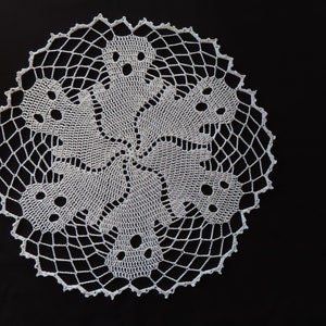 May include: White crocheted doily with a design of six ghosts in a circular pattern.