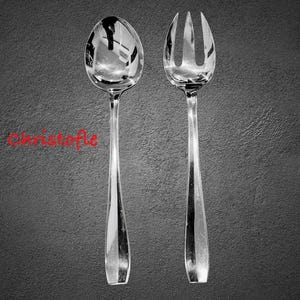May include: A silver serving spoon and fork set with long, slender handles. The spoon has a rounded bowl, and the fork has three tines. The word "Christofle" is written in red cursive. The set is displayed against a dark gray background.