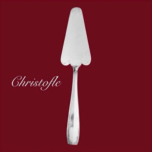 May include: A silver cake server with a scalloped edge and a long, slender handle. The word "Christofle" is written in cursive on the left side of the image. The server is set against a deep red background.