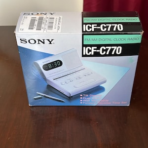 May include: A white ceramic mug with a black handle and the text "But First, Coffee" in a bold, black font. The mug is set against a neutral background, highlighting its simple design.