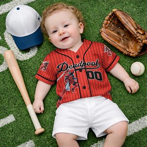 May include: A baby wearing a red and black pinstripe baseball jersey with the word "Deadpool" and the number "00" on the front. The baby is also wearing white shorts. A baseball bat, baseball glove, baseball, and a white and blue baseball cap are nearby.
