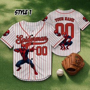 Może przedstawiać: Biała koszulka baseballowa z czerwonymi prążkami, z napisem "Spiderman" i numerem "00" w kolorze czerwonym. Koszulka ma grafikę Spidermana z przodu i z tyłu. Widoczna jest r&oacute;wnież rękawica i piłka do baseballu.