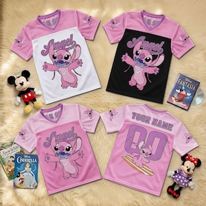 May include: Pink and white short-sleeved jersey shirts featuring the character Angel from Lilo & Stitch. One shirt has the name "Angel" printed on the front, while another has "YOUR NAME" and the number "00". Other Disney merchandise is also visible.