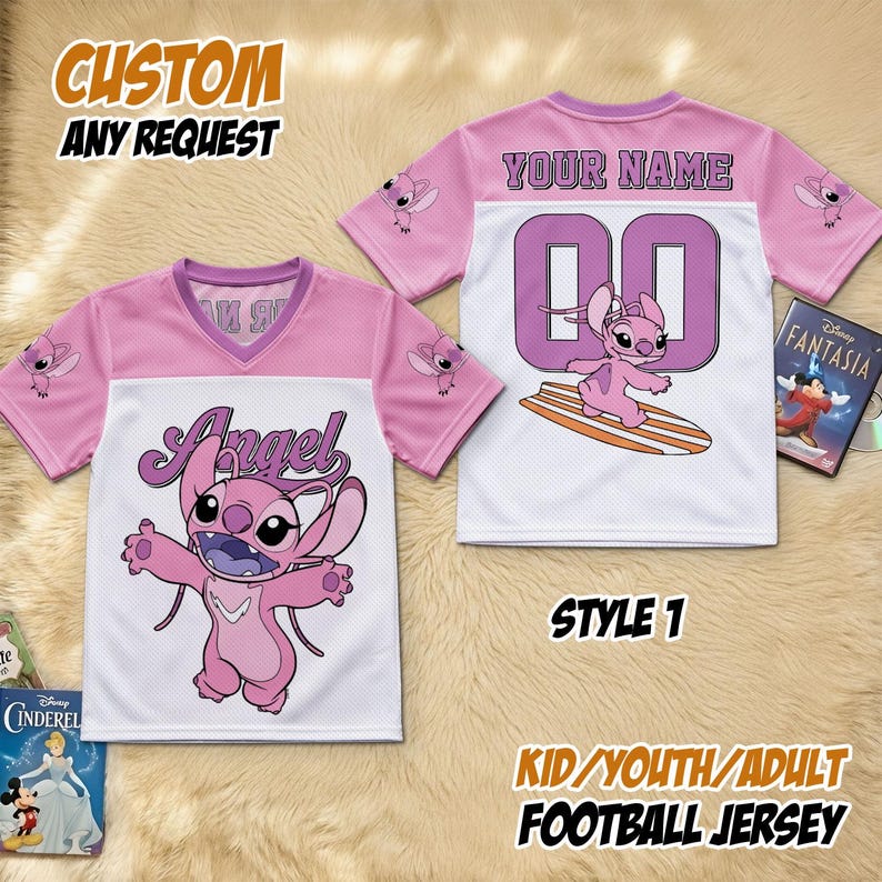 May include: Pink and white football jersey featuring the word "Angel" and a cartoon character on the front. The back displays "YOUR NAME" and the number "00". The jersey is labelled "STYLE 1" and "KID/YOUTH/ADULT FOOTBALL JERSEY".