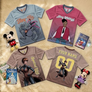 Op de afbeelding: Vier V-hals T-shirts met cartoonafbeeldingen en tekst. Eén shirt is lichtblauw met een eekhoorn, een ander is roze met een illustratie van een persoon, en twee zijn bruin met een Squirrel Girl-illustratie. Disney-boeken en knuffels zijn ook aanwezig.