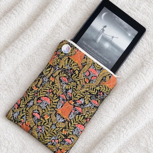 May include: A quilted fabric sleeve featuring a black background with a dense pattern of orange mushrooms, green ferns, and white foliage. A black e-reader is partially inserted into the sleeve, displaying the text Your next great read is waiting.
