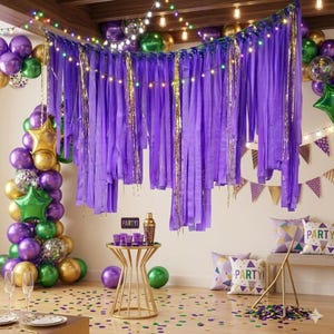 May include: A purple fringe backdrop with gold tinsel accents, decorated with string lights. A gold metal table holds purple cups and a shaker. A balloon arch features purple, green, and gold balloons, including star shapes. Pillows with the word PARTY are present.