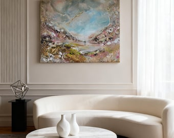 May include: A rectangular landscape painting featuring a textured impasto technique with a central sailboat on water, surrounded by abstract hills in shades of blue, pink, gold, and brown, framed in a thin gold border and hung on a beige wall.