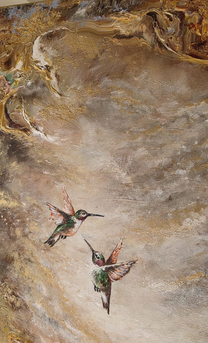 May include: An oil painting on canvas featuring two hummingbirds in flight against a textured background of swirling gold, bronze, and cream tones. The birds display iridescent green and red plumage, captured with thick, visible brushstrokes.