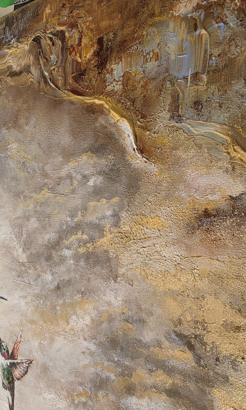 May include: A textured abstract painting on canvas featuring a hummingbird in the lower left corner. The artwork displays a layered composition of metallic gold, deep brown, and muted gray tones with thick, visible brushstrokes and impasto paint.