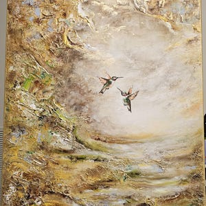 May include: A rectangular canvas painting featuring two hummingbirds in flight against a textured, abstract background. The artwork utilizes a palette of gold, cream, brown, and muted green tones with heavy impasto paint application and metallic accents.
