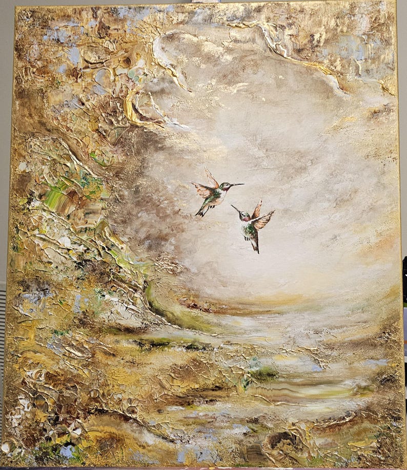 May include: A rectangular canvas painting featuring two hummingbirds in flight against a textured, abstract background. The artwork utilizes a palette of gold, cream, brown, and muted green tones with heavy impasto paint application and metallic accents.