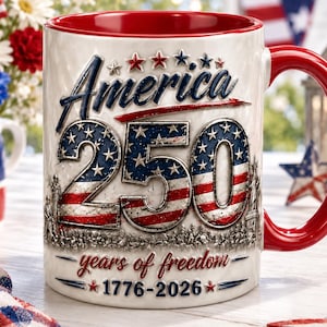 May include: A white ceramic mug with a red interior and handle, featuring the text "America 250" in blue and red, with stars and stripes design. The mug also includes the words "years of freedom" and the dates 1776-2026. Patriotic theme.
