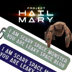 May include: Two keychains with the text "I AM SCARY SPACE MONSTER YOU ARE LEAKY SPACE BLOB" and "I AM SCARY SPACE YOU ARE LEAKY". The keychains are green and blue. The image also features a brown, robotic-looking creature and the words "PROJECT HAIL MARY".