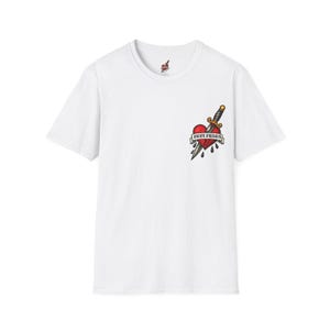 Puede incluir: Camiseta blanca con un diseño estilo tatuaje en la parte delantera. El diseño incluye un corazón rojo atravesado por una daga, con las palabras "HOPE FRIENDS" en una pancarta. Un pequeño gráfico de corazón está en la parte superior de la espalda.