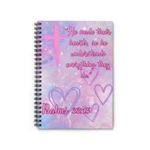 May include: A spiral-bound notebook with a purple and pink galaxy-themed cover. The cover features a pink cross, hand-drawn heart outlines, and the text: "He made their hearts, so he understands everything they do." and "Psalms 33:15".