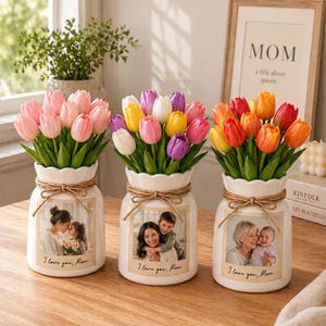 Può includere: Tre vasi in ceramica bianca con bouquet di tulipani rosa, multicolore e arancione. Ogni vaso presenta una foto di famiglia e il testo "I love you, Mom". I vasi sono legati con spago e poggiano su una superficie di legno.
