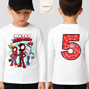 Puede incluir: Camiseta blanca de manga larga con el texto "MATEO and the Amazing Friends" y personajes de dibujos animados de Spider-Man. La parte trasera muestra un n&uacute;mero 5 rojo con un dise&ntilde;o de telara&ntilde;a.