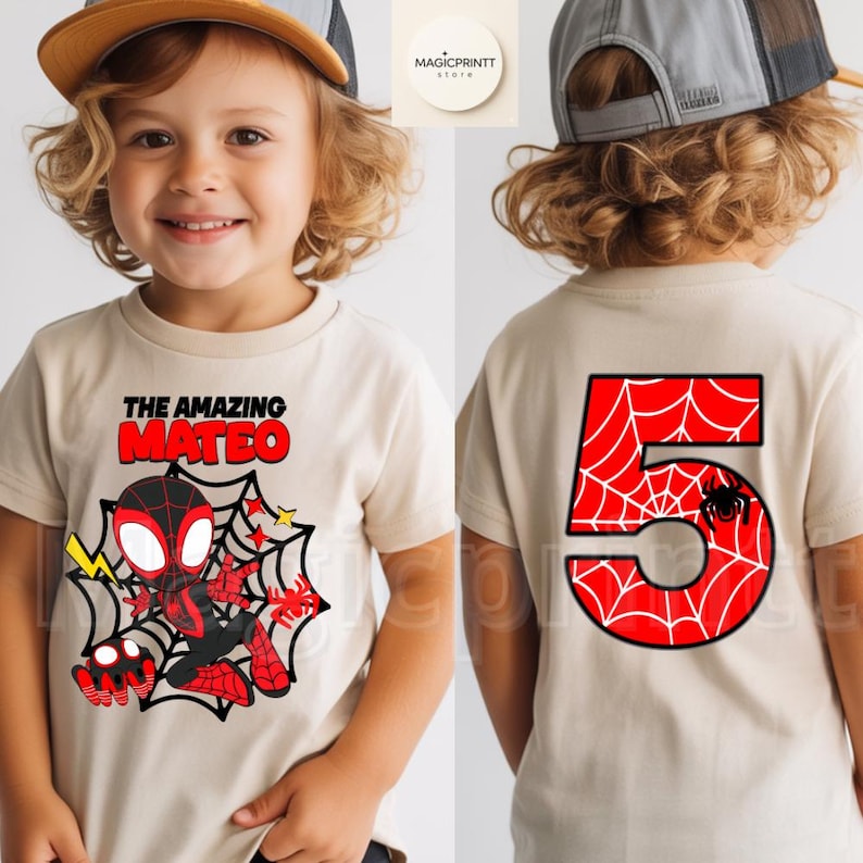 May include: A tan t-shirt featuring a cartoon Spider-Man design with the text "THE AMAZING MATEO" in red and black. The back of the shirt displays a large red number 5 with a spiderweb design and a black spider. The shirt is for a child.