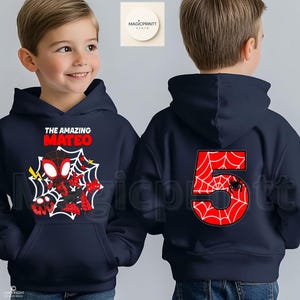 May include: Navy blue hooded sweatshirt featuring a Spider-Man graphic with the text "THE AMAZING MATEO" on the front. The back displays a large red number 5 with a spiderweb design and a small spider. The sweatshirt is designed for children.