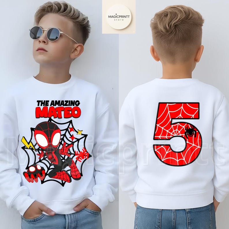 May include: White sweatshirt featuring a graphic of a superhero with the text "THE AMAZING MATEO" on the front. The back of the sweatshirt displays a large red number "5" with a spiderweb design and a small spider.