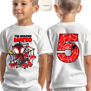 May include: White t-shirt featuring a cartoon Spider-Man design with the text "THE AMAZING MATEO" on the front. The back of the shirt displays a large red number 5 with a spiderweb pattern and a spider.