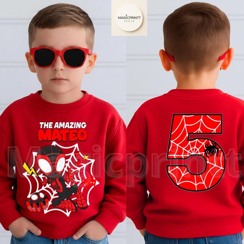 May include: Red sweatshirt featuring a Spider-Man graphic with the text "THE AMAZING MATEO" on the front. The back displays a large number "5" with a spiderweb design and a spider. The child is wearing red sunglasses.