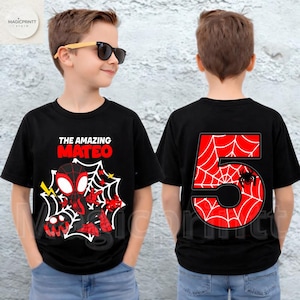 May include: Black t-shirt featuring a graphic of a superhero with the text "THE AMAZING MATEO" and a spider web design. The back of the shirt displays a large red number "5" with a spider web pattern and a spider.