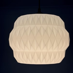 Puede incluir: Una lámpara colgante blanca y geométrica con un patrón de diamantes. La luz cuelga de un cable negro sobre un fondo azul oscuro. La lámpara tiene una forma redondeada con una superficie texturizada, adecuada para la iluminación interior.