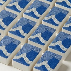 American mahjong tile set with custom blue and white coral and shell print backs, fanned out to show front faces and matching backs — a complete mah jongg tile set built for serious play, included with a coordinating coastal mahjong mat, card holders, and tile bag.